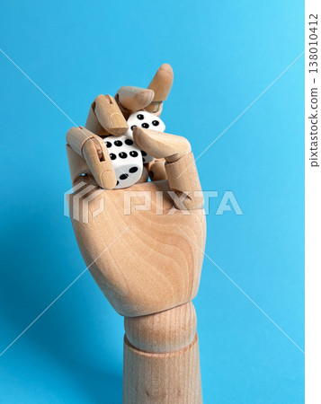 Wooden hand holds two dice against a blue background in a creative setup for games and chance 138010412