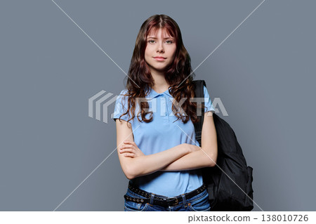 Portrait of smiling confident teenage girl with crossed arms, backpack on gray background 138010726