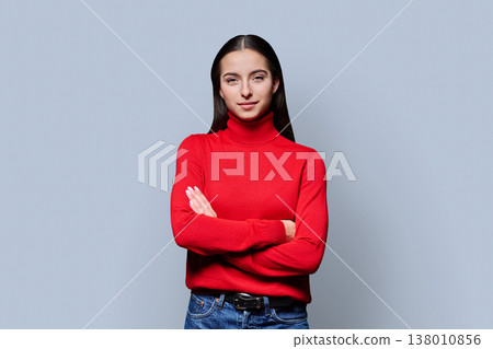 Beautiful young woman with crossed arms looking at camera on grey background 138010856