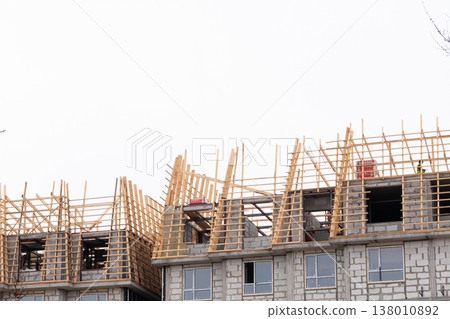 Unfinished residential building under construction with wooden roof framing. Concrete block structure with timber rafters and a construction worker. Copy space for text Unfinished residential building under construction with wooden roof framing. Concrete block structure with timber rafters and a construction worker. Copy space for text 138010892