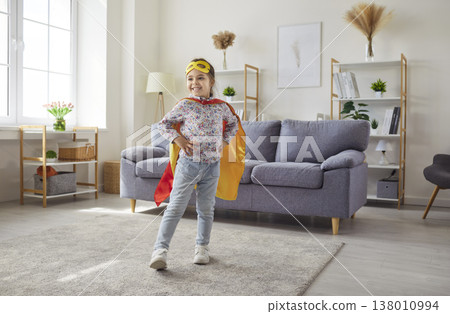 Portrait of child girl in super hero costume standing in the living room at home and smiling 138010994