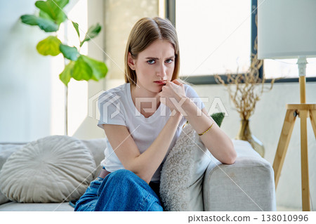 Sad unhappy stressed young woman sitting at home on sofa 138010996