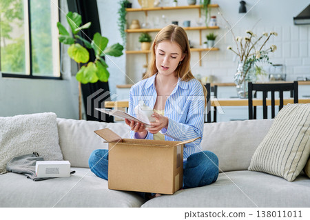 Young happy woman unpacking cardboard box with online order 138011011