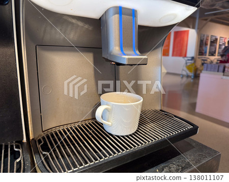 Coffee machine dispensing drink into white cup on metal grid surface. Morning routine, self service, quick break, urban convenience, everyday habit, modern appliance usage 138011107