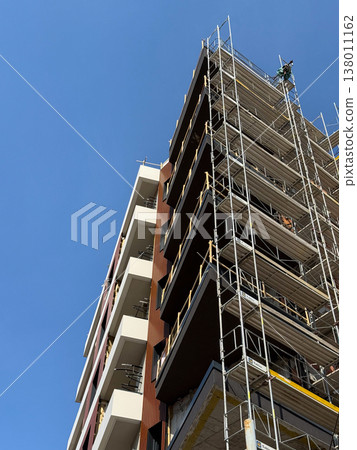 High building under construction with scaffolding and crane against blue sky. Urban development, architecture progress, engineering process, infrastructure growth, city expansion, modern industry 138011162