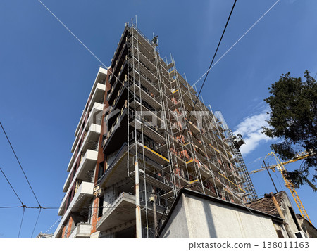 High building under construction with scaffolding and crane against blue sky. Urban development, architecture progress, engineering process, infrastructure growth, city expansion, modern industry High building under construction with scaffolding and crane against blue sky. Urban development, architecture progress, engineering process, infrastructure growth, city expansion, modern industry 138011163