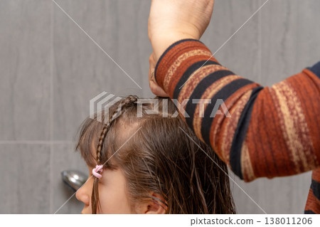 Mother's hands gather a section of a girl's hair for braiding in the bathroom. Mother's hands gather a section of a girl's hair for braiding in the bathroom. 138011206
