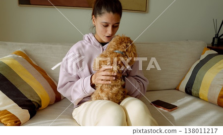 Serene indoor moment where woman gently cuddles her poodle at night Serene indoor moment where woman gently cuddles her poodle at night 138011217