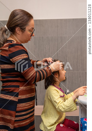 Woman styles a young girl's wet hair near the sink in a home bathroom. Woman styles a young girl's wet hair near the sink in a home bathroom. 138011228