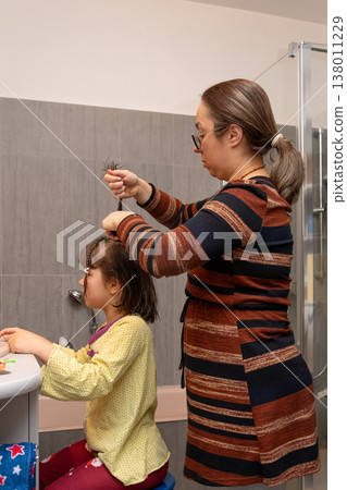 Mother gathers and braids her daughter's hair after washing in a modern bathroom. Mother gathers and braids her daughter's hair after washing in a modern bathroom. 138011229