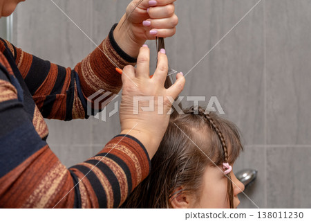Close up of a woman braiding a young girl's hair during home grooming. Close up of a woman braiding a young girl's hair during home grooming. 138011230