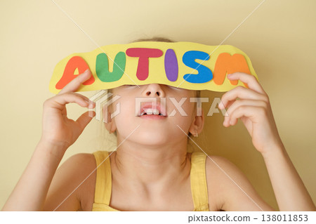 A child with an autism spectrum disorder hides behind a cardboard sign with a diagnosis. Developmental disorder affecting communication, social interaction, and perception of the world A child with an autism spectrum disorder hides behind a cardboard sign with a diagnosis. Developmental disorder affecting communication, social interaction, and perception of the world 138011853