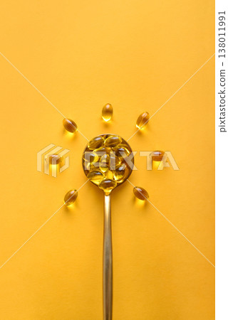 Golden spoon with soft gels vitamin D (cholecalciferol) in shape of sun 138011991