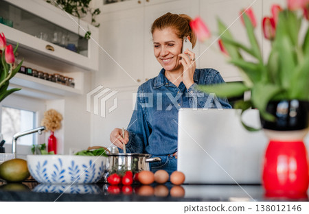 Mature woman making phone call while cooking in kitchen. 138012146