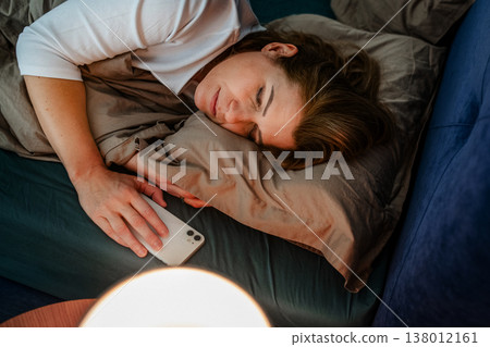 Tired middle aged woman sleeping in bed after using smartphone. 138012161
