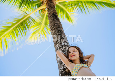 Smiling girl by palm tree during tropical family vacation. Smiling girl by palm tree during tropical family vacation. 138012189