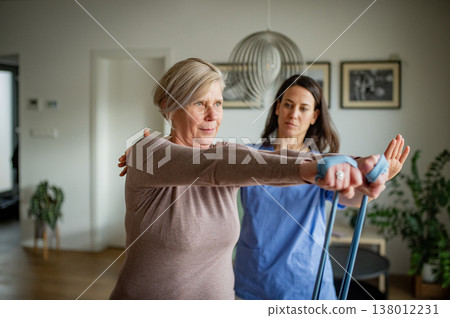 Physiotherapist guiding senior woman during resistance band exercise. Physiotherapist guiding senior woman during resistance band exercise. 138012231