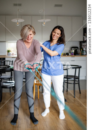 Physiotherapist guiding senior woman during resistance band exercise. Physiotherapist guiding senior woman during resistance band exercise. 138012234
