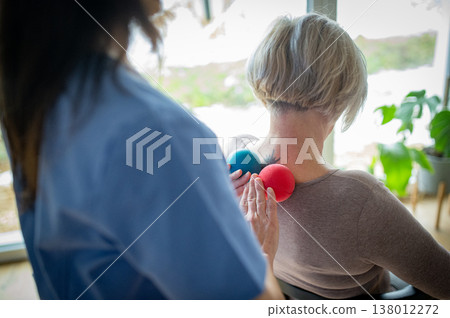 Physiotherapist helping senior woman with neck exercise, home therapy session. 138012272
