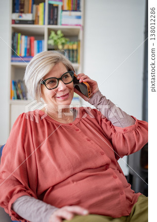 Older woman talking on phone while working from home during retirement. Older woman talking on phone while working from home during retirement. 138012286