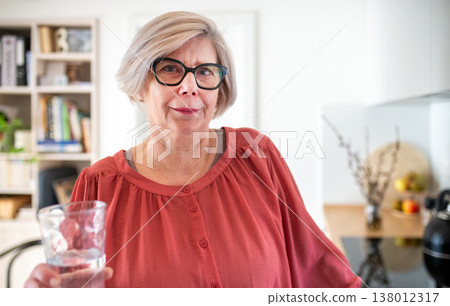 Senior woman holding glass of water at home in kitchen. Senior woman holding glass of water at home in kitchen. 138012317