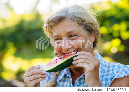 Lovely senior woman eating slice of watermelon in garden. 138012334