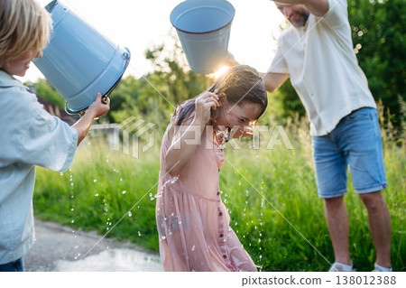 Father and son pouring water on girls during Easter Monday tradition. Father and son pouring water on girls during Easter Monday tradition. 138012388