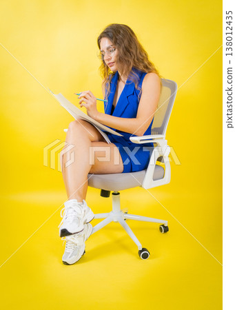 Woman writing notes with pencil on vibrant yellow background Woman writing notes with pencil on vibrant yellow background 138012435