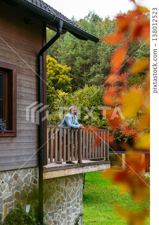 Man is enjoying a relaxing, peaceful moment at home, standing on patio, looking at autumn nature around him. Man is enjoying a relaxing, peaceful moment at home, standing on patio, looking at autumn nature around him. 138012523