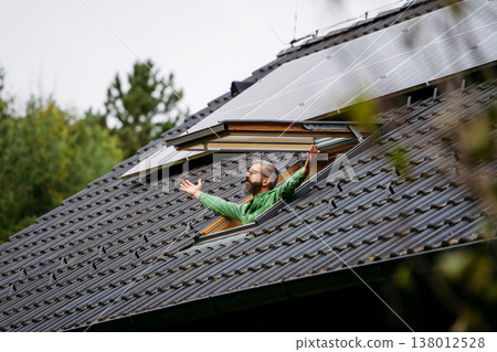 Man looking from skylight, roof window with solar panels above him. Sustainable lifestyle and green household. 138012528
