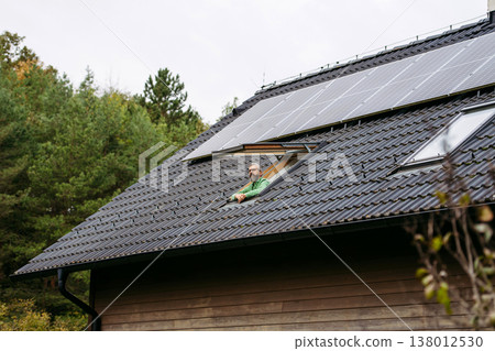 Man looking from skylight, roof window with solar panels above him. Sustainable lifestyle and green household. Man looking from skylight, roof window with solar panels above him. Sustainable lifestyle and green household. 138012530