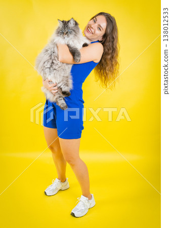 Happy young woman holding fluffy cat against yellow 138012533