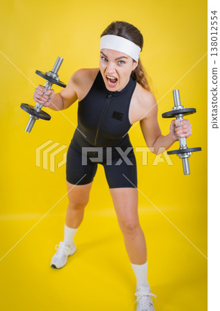 Woman showing intense effort lifting dumbbells Woman showing intense effort lifting dumbbells 138012554