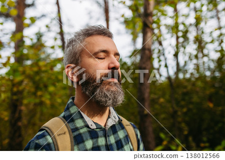 Handsome man standing in the middle of nature with closed eyes, enjoying peaceful atmosphere of the forest, forestbathing. Handsome man standing in the middle of nature with closed eyes, enjoying peaceful atmosphere of the forest, forestbathing. 138012566