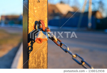 Rusty padlock on a metal chain secured to a post at sunset. Rusty padlock on a metal chain secured to a post at sunset. 138012938