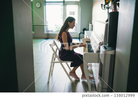 Young woman in purple dress playing white upright piano in bright studio Young woman in purple dress playing white upright piano in bright studio 138012999