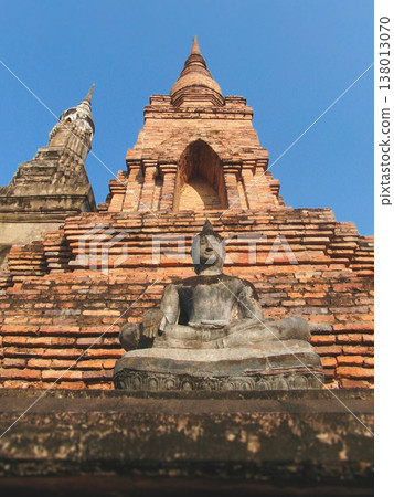 Low angle view of ancient Buddha statue and stone stupa at Wat Mahathat Sukhothai 138013070