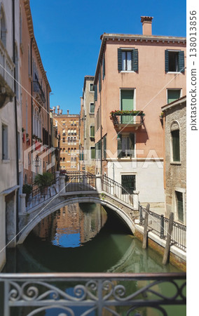 Scenic view of a small arched stone bridge crossing a narrow canal with historic Venetian houses 138013856