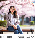 A relaxing spring image portrait: sitting on a bench and smiling in a park filled with cherry blossoms in full bloom. 138013872