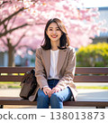 A refreshing spring portrait of a woman smiling while sitting on a bench amidst a row of cherry trees in full bloom. 138013873