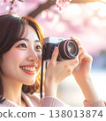 A spring portrait shoot: A smiling woman holding a camera under cherry blossoms in full bloom, bathed in the setting sun. 138013874