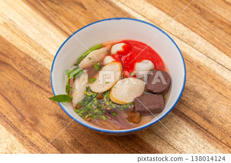 Bowl of thai noodle soup with fish balls pork blood herbs and broth on wooden table showing traditional street food flavor rich taste and authentic cuisine 138014124