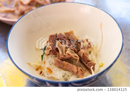 Thai dry noodles topped with pork and offal in bowl on table showing traditional street food texture rich flavor and authentic asian cuisine experience Thai dry noodles topped with pork and offal in bowl on table showing traditional street food texture rich flavor and authentic asian cuisine experience 138014125