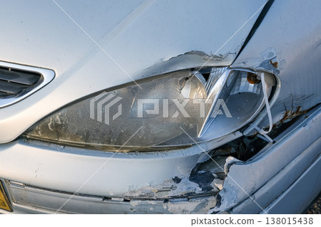 Damaged car headlight and broken front bumper after road accident closeup with cracked plastic and scratched white vehicle body. Damaged car headlight and broken front bumper after road accident closeup with cracked plastic and scratched white vehicle body. 138015438