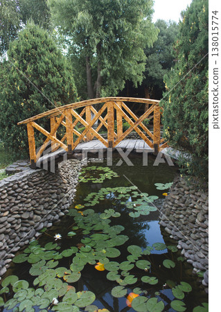 Decorative wooden footbridge over a lily pond in a lush garden Decorative wooden footbridge over a lily pond in a lush garden 138015774