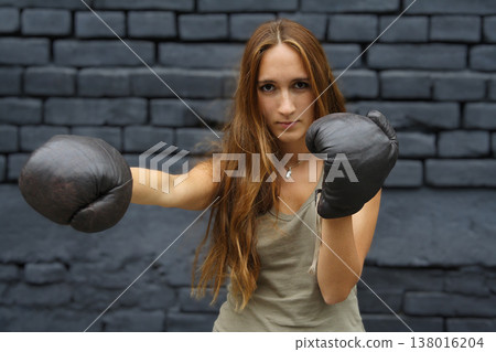 Young woman in boxing gloves throwing a punch against dark brick wall Young woman in boxing gloves throwing a punch against dark brick wall 138016204