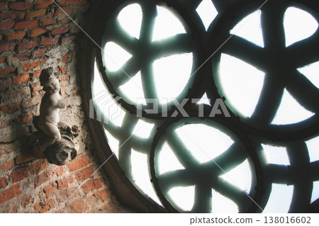 Stone cherub sculpture beside a decorative rose window in a brick wall Stone cherub sculpture beside a decorative rose window in a brick wall 138016602