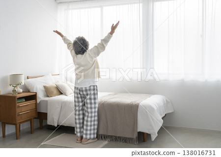 The back view of a senior woman taking a deep breath in front of her bed. The back view of a senior woman taking a deep breath in front of her bed. 138016731