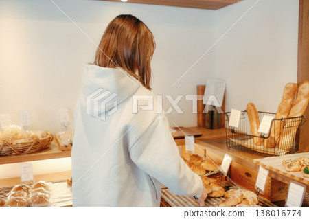 A woman in her 20s, seen from behind, choosing bread at a bakery. A woman in her 20s, seen from behind, choosing bread at a bakery. 138016774