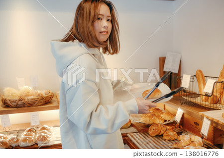A woman in her 20s, seen from behind, choosing bread at a bakery. 138016776